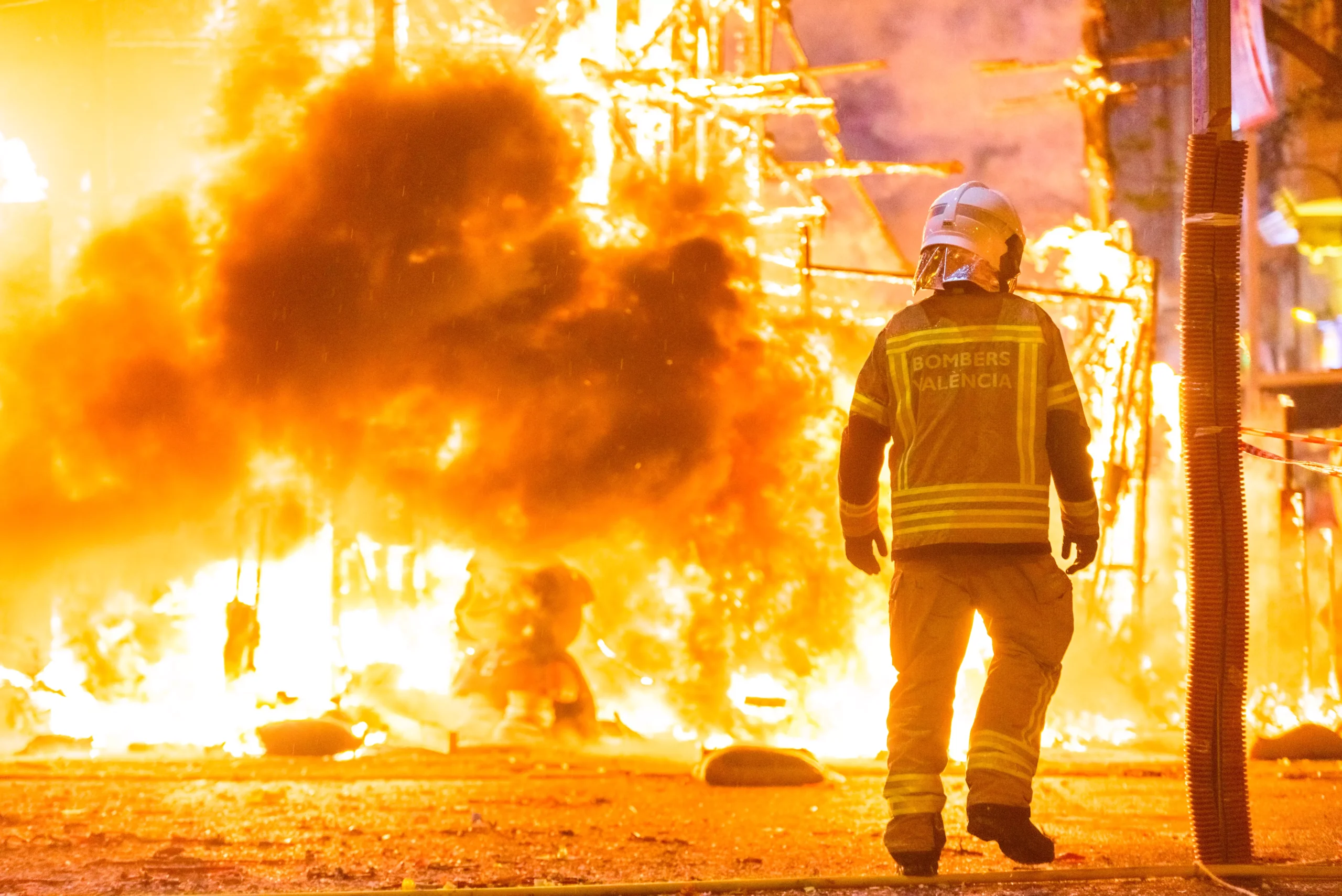 firefighter in protective gear walks in front of a large fire